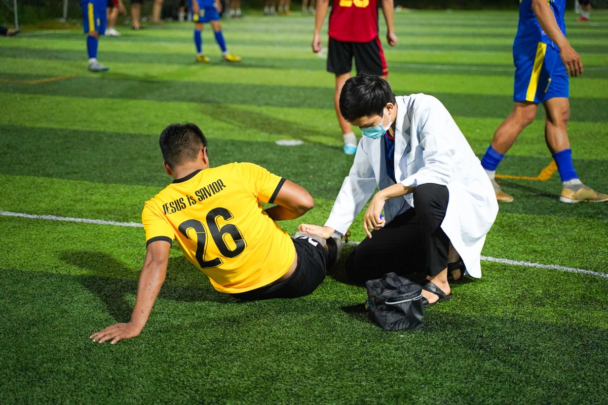 Sports medicine physician kneeling to examine an injured soccer player's ankle on the field during a match