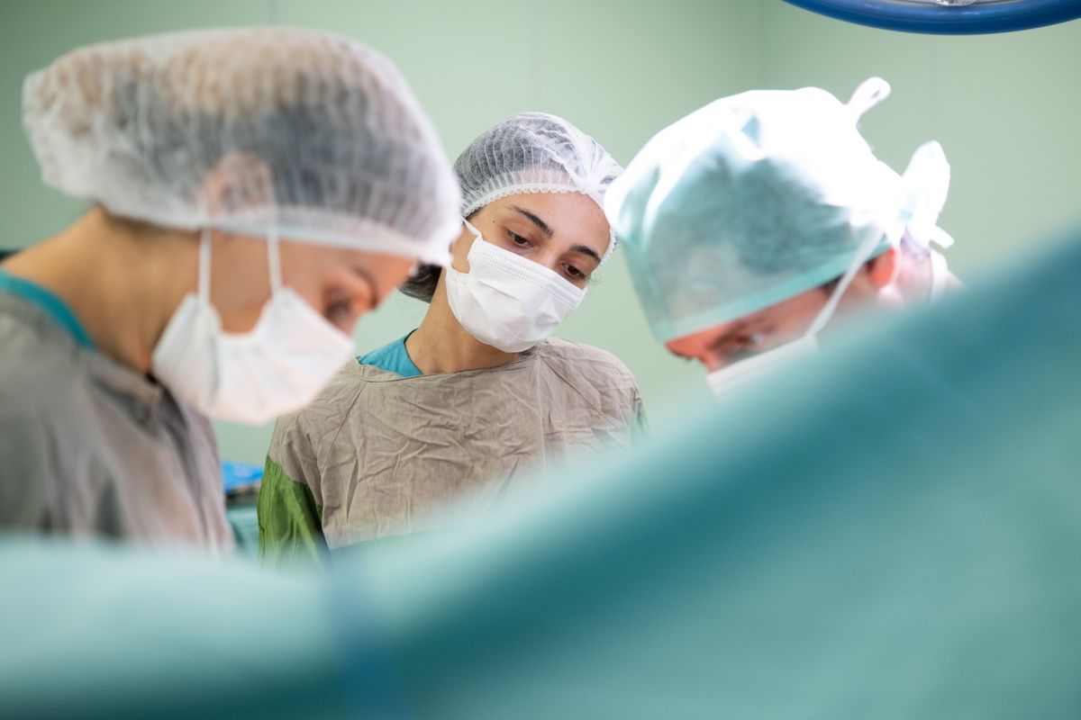 Surgical team in masks and scrub caps focused on a procedure under operating room lights