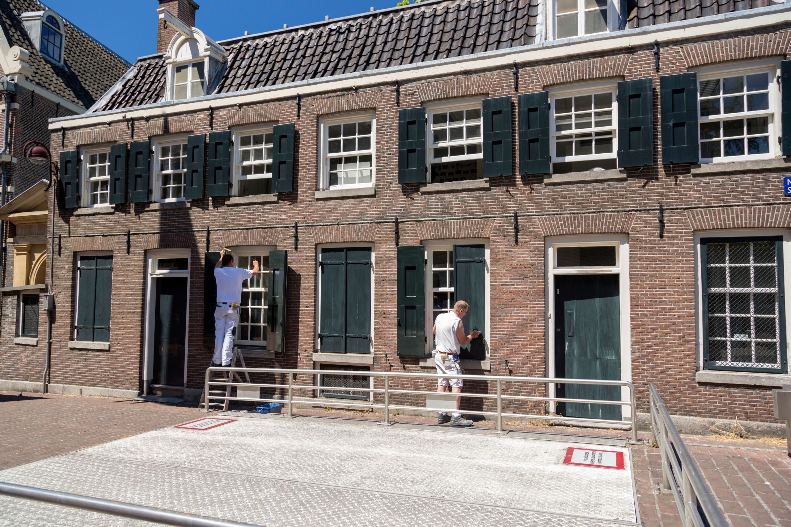 Two painters refurbishing a brick house facade on a sunny day