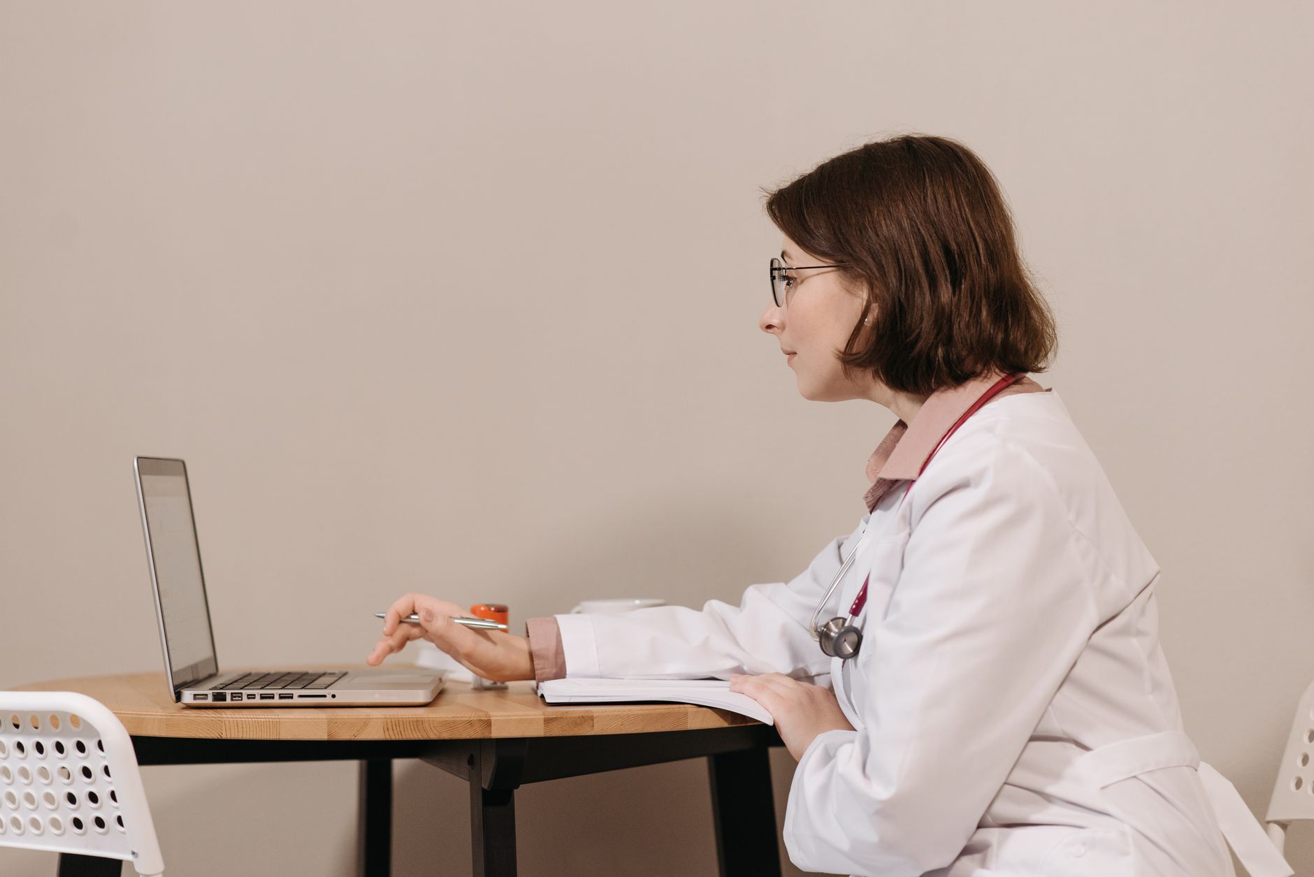 Doctor in a white coat reviewing patient information on a laptop at a clinic desk