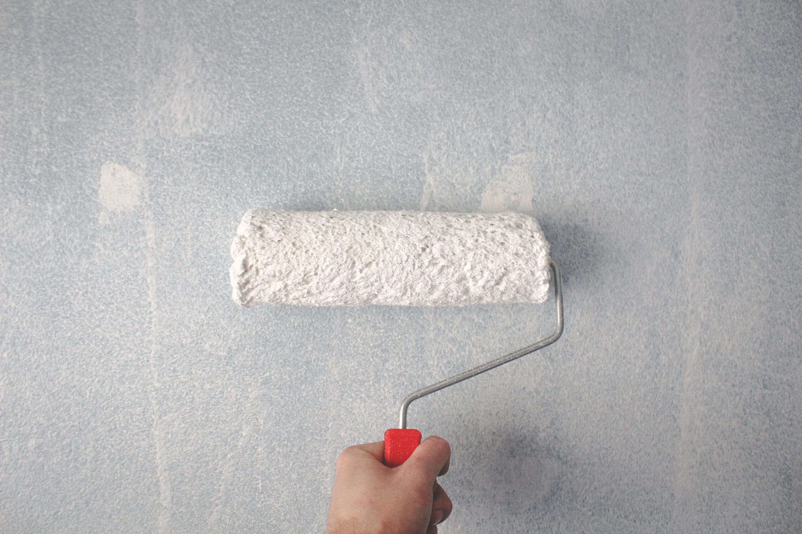 A hand using a paint roller to apply white paint to a wall, SEO for painting contractors