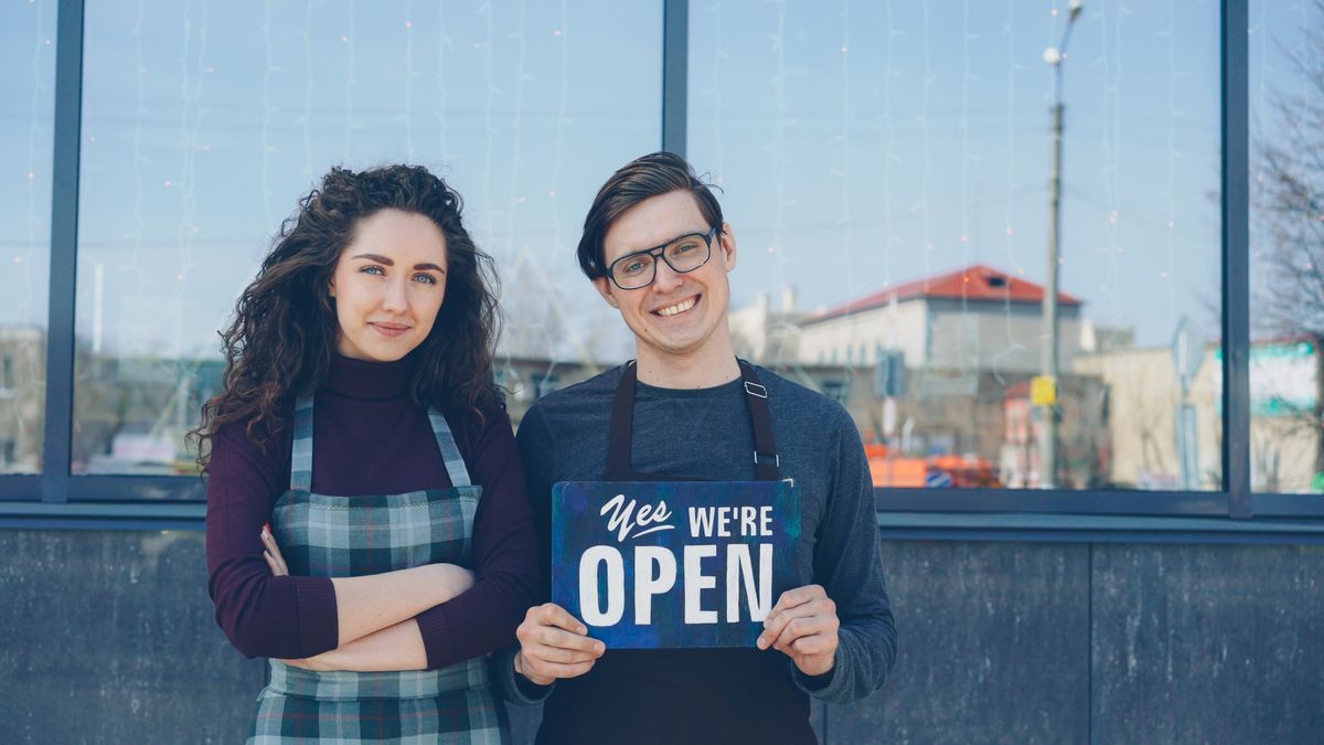 Two small business owners smiling while holding an open sign outside their shop