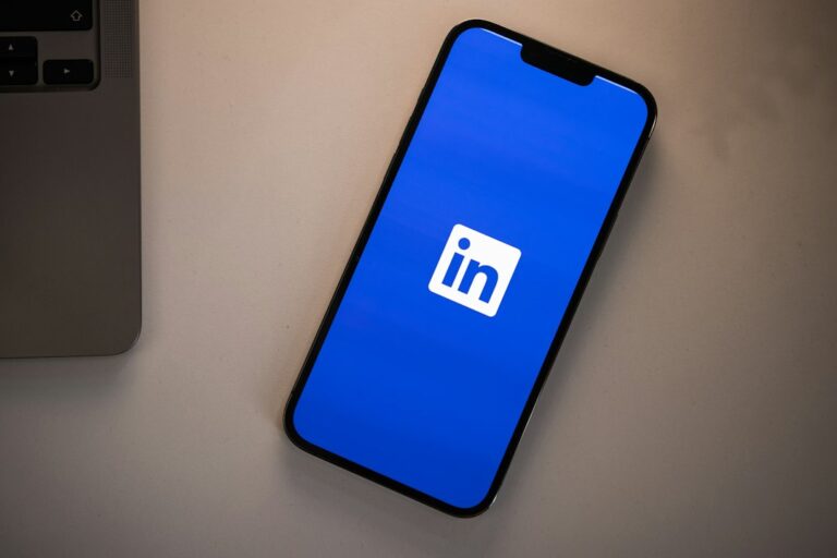Smartphone displaying the LinkedIn app logo on a blue screen next to a laptop