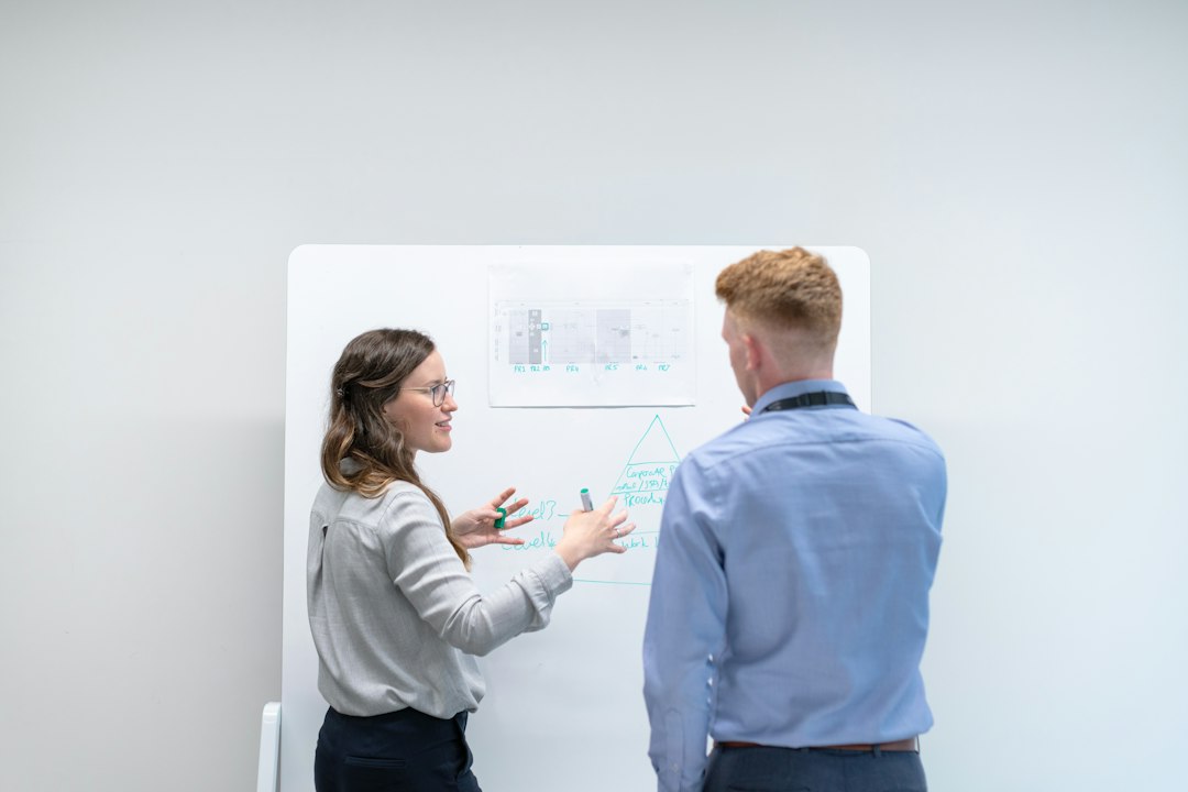 Two colleagues discussing a project in front of a whiteboard in an office